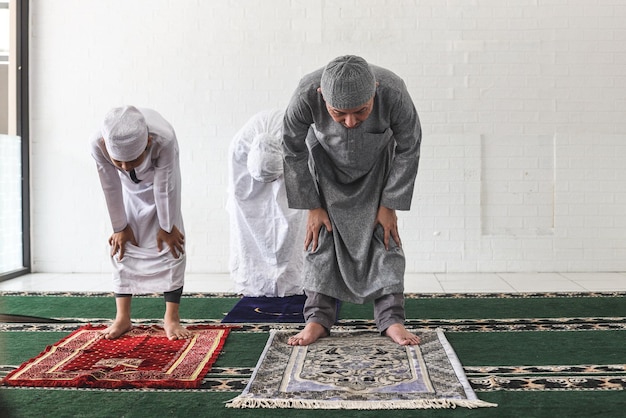 A família muçulmana asiática está ajoelhada e rezando juntos na mesquita