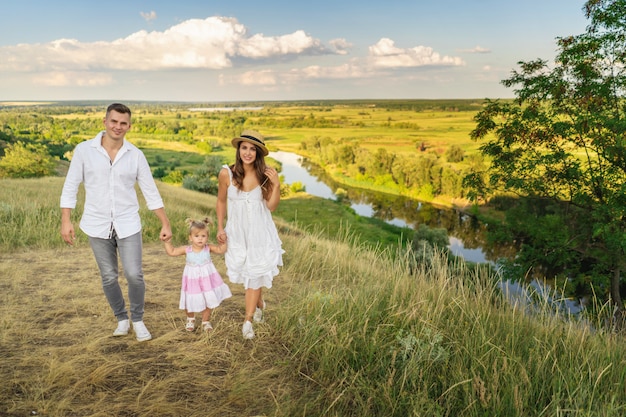 A família nova feliz que passa o tempo junto, correndo lá fora, entra na natureza, em férias, ao ar livre. O conceito de férias em família.