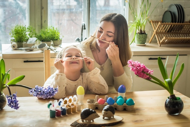 A família pinta ovos de páscoa coloridos, mãe e filha celebram juntos o feriado da primavera