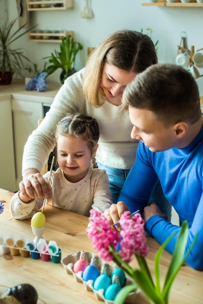 A família pinta ovos de páscoa coloridos, mãe, pai e filha celebram o feriado da primavera juntos, jovem, homem e menina, colorindo o cenário tradicional