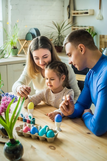 A família pinta ovos de páscoa coloridos, pai e filha comemoram o feriado de primavera juntos