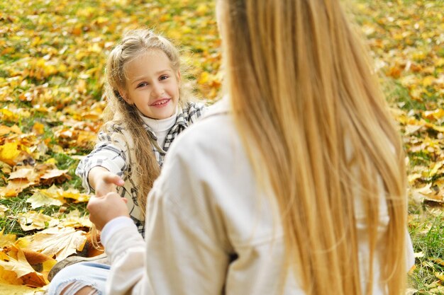 A família se diverte no parque A menina e a mãe sentam em um cobertor e descansam A filha olha para a câmera e sorri Foto horizontal