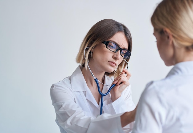 A faxineira em um vestido médico ouve os batimentos cardíacos do paciente em um fundo claro