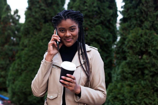 A feliz mulher afro-americana na rua com telefone e café