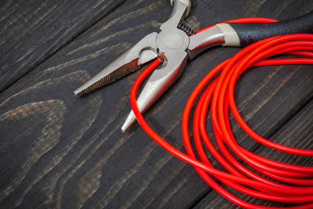 A ferramenta do eletricista e o fio vermelho em placas de madeira pretas para consertar sistemas energizados ou comunicações