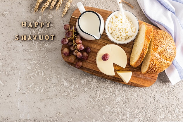 A festa da doação da Torá produtos lácteos pão uvas o conceito do feriado judaico fundo cinza com letras feliz shavuot