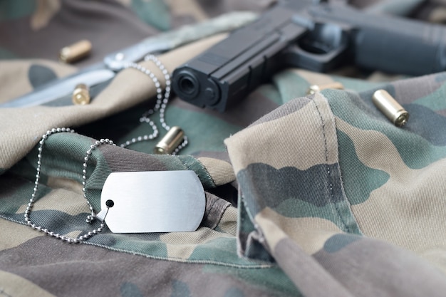 A ficha de identificação do Exército com balas de 9 mm e pistola repousa sobre tecido verde camuflado dobrado. Um conjunto de itens militares veteranos ou um kit de troféus antigo