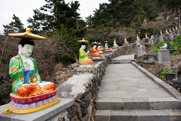 A figura colorida do deus chinês e a estátua do buda do anjo da divindade nas escadas de pedra vão para a montanha Sanbangsa para os viajantes coreanos que viajam visitam o respeito rezando no templo Sanbangsa em Jeju na Coreia do Sul