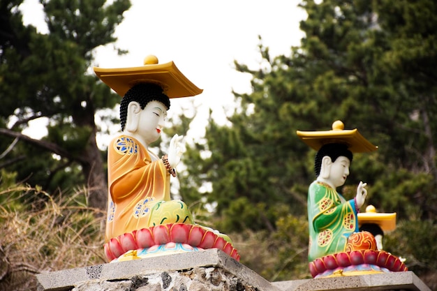 A figura colorida do deus chinês e a estátua do buda do anjo da divindade nas escadas de pedra vão para a montanha Sanbangsan para os viajantes coreanos que viajam visitam o respeito rezando no Templo Sanbangsa em Jeju na Coreia do Sul