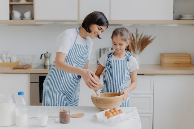 A filha e a mãe adoram cozinhar, vestidas com aventais listrados, preparam um jantar delicioso, usam ingredientes diferentes, têm rotina na cozinha, ficam em casa.