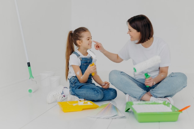 A filha e a mãe amigáveis positivas esfregam-se com tinta branca