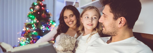 A filha e os pais deitaram na cama e leram um livro perto da árvore de natal