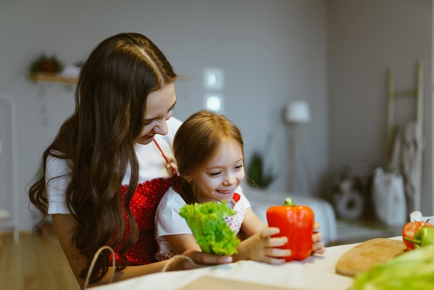 A filha se senta nos braços da mãe e elas separam os vegetais na cozinha