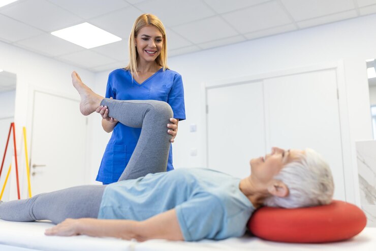 Foto a fisioterapeuta está a ajudar uma mulher idosa a esticar o tendão da coxa e a fazer reabilitação da coxa ou da perna na sala de ginástica. ela está deitada numa cama de massagem.