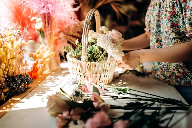 A florista coleta um buquê na cesta de peônias frescas e rosas na floricultura.