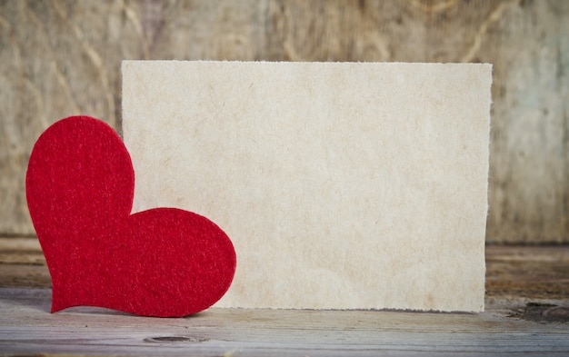 A forma de um cartão na mesa de madeira. O coração feito à mão de feltro vermelho está no canto esquerdo do formulário