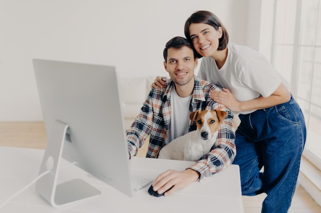 A foto do freelancer masculino trabalha remotamente no computador com o cachorro que sua esposa afetuosa abraça e ajuda com algumas perguntas colocadas em uma grande sala no local de trabalho, discutindo alguns problemas e o orçamento familiar