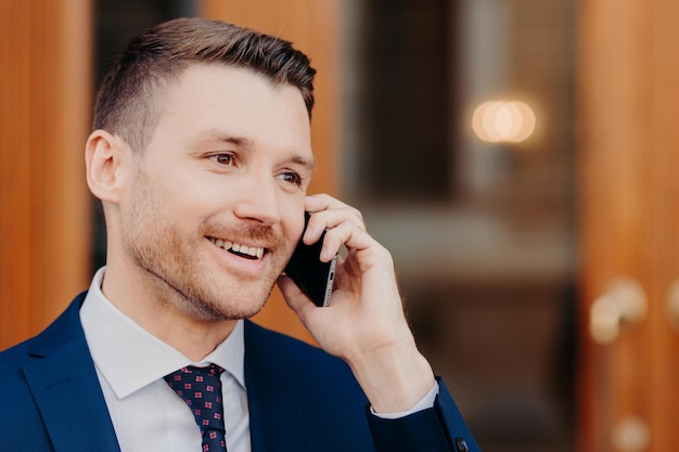 A foto lateral de um jovem bonito fala em roaming via telefone celular tem expressão positiva parece pensativamente de lado com espaço de cópia para informações de negócios Conceito de pessoas e conversa