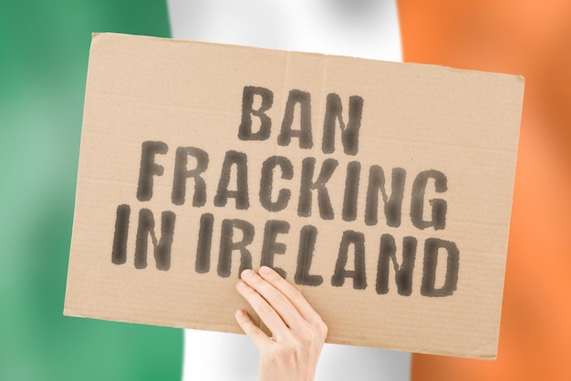 A frase Ban fracking na Irlanda está em um banner nas mãos dos homens com uma bandeira irlandesa borrada ao fundo Pipeline Resource Dinheiro Política Poluição Lucro Petrol Pumping Crude