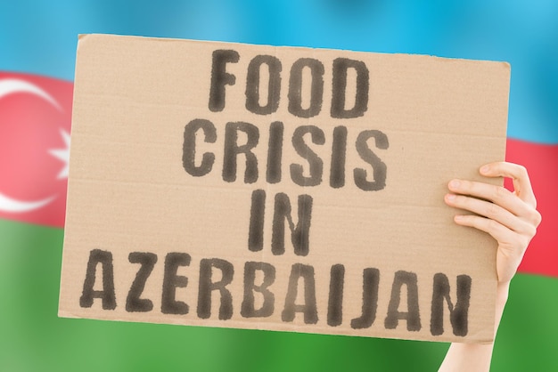 A frase Crise alimentar no Azerbaijão está em um banner nas mãos dos homens com uma bandeira do Azerbaijão borrada ao fundo Crise Finanças Vida Nutrição Pão Desastre Desastre Questão social