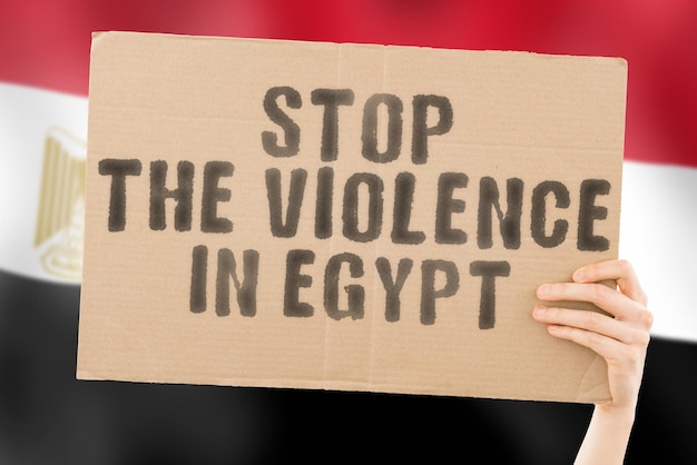A frase Pare a violência no Egito está em um banner nas mãos dos homens com uma bandeira egípcia borrada ao fundo Triste Direitos Segurança Social Estresse Combate Ódio Crueldade Furioso Bater