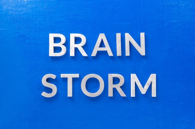 A frase tempestade cerebral colocada com letras de metal prateado no quadro azul em postura plana com composição central