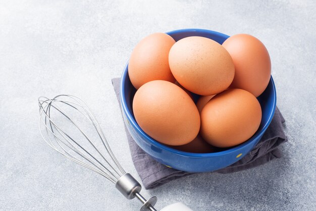 A galinha crua de Brown eggs em uma bacia azul em um fundo cinzento.