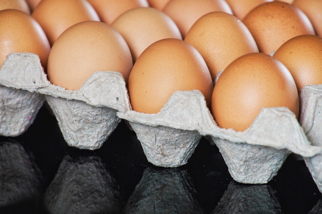 A galinha fresca eggs na bandeja de papel cinzenta (pacote do cartão) na tabela preta do espelho.