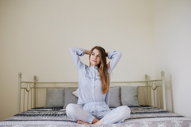 A garota acordou e sentou em seu pijama na cama em seu quarto. Interior cinza-branco elegante. A garota se alonga.