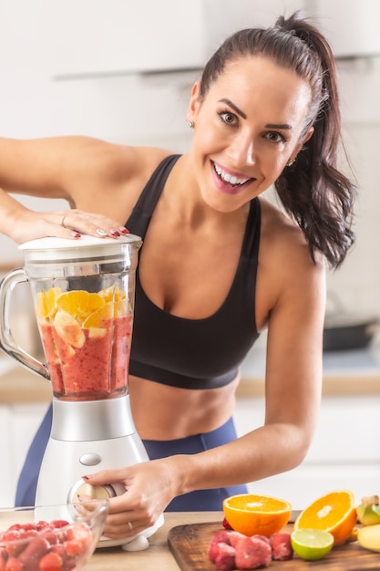 A garota apta faz comida de fitness misturando frutas cítricas em um smoothie.