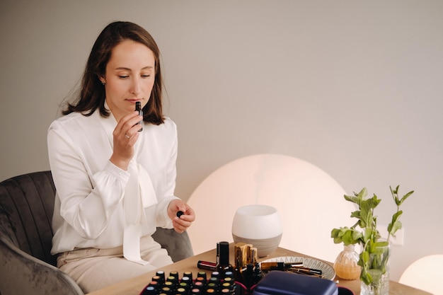A garota aromaterapeuta está sentada em seu escritório e segurando uma garrafa de óleos aromáticos, há óleos essenciais na mesa