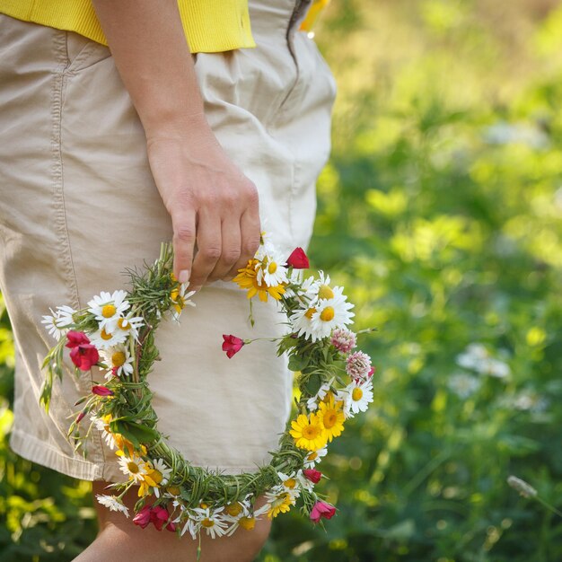 A garota caminha no parque com uma coroa de flores nas mãos primavera no parque