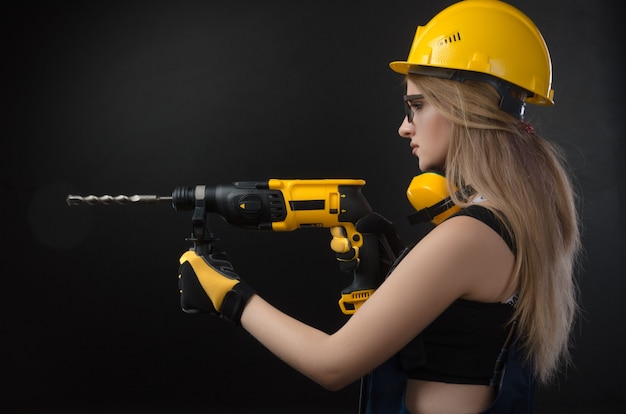 A garota com roupas de construção e equipamentos de proteção, posando com um martelo