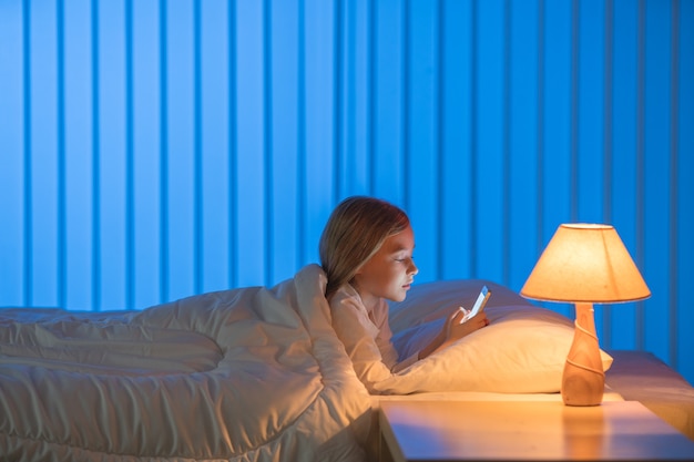 A garota com um telefone estava deitada na cama. Noite noite