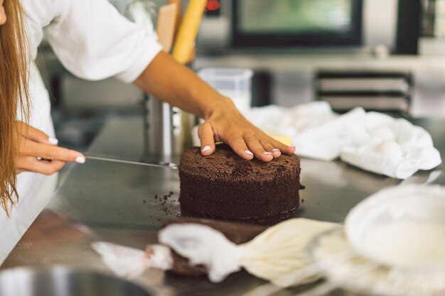 A garota da confeiteira está preparando um biscoito de bolo com creme branco e bolos de chocolate para cozinhar