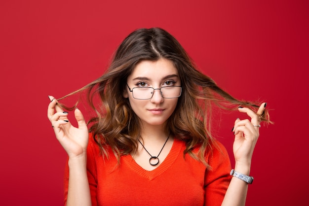 A garota de óculos torce o cabelo com os dedos em um vermelho.