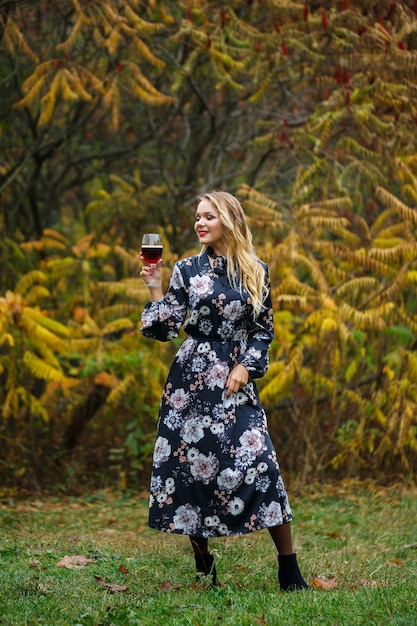 A garota de vestido segura uma taça de vinho tinto na floresta de outono