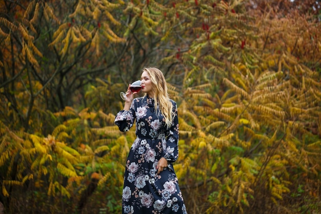 A garota de vestido segura uma taça de vinho tinto na floresta de outono