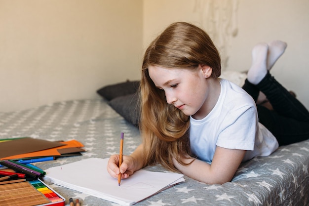 A garota depois da escola brinca em casa desenha com lápis e canetas hidrográficas