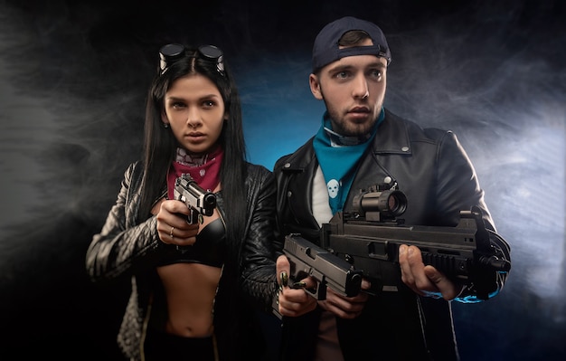 A garota e um cara em uma jaqueta de couro com uma arma