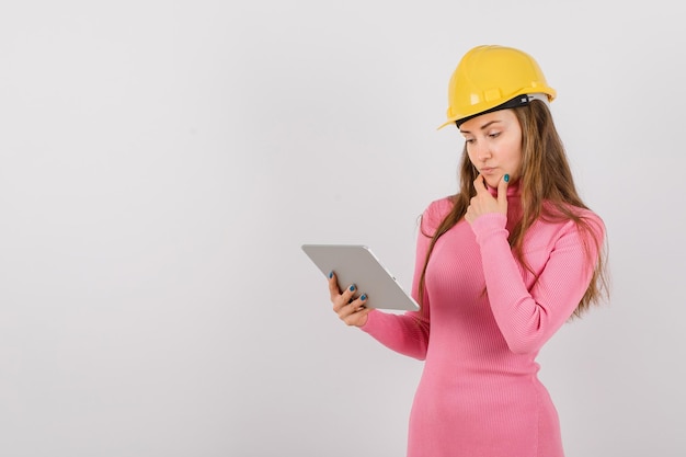 A garota engenheira está pensando olhando para o computador tablet na mão sobre fundo branco
