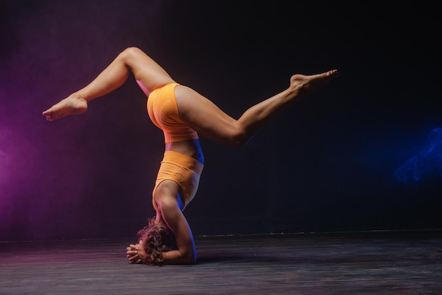 A garota está envolvida em esticar em um fundo escuro uma foto elegante de fitness e ioga