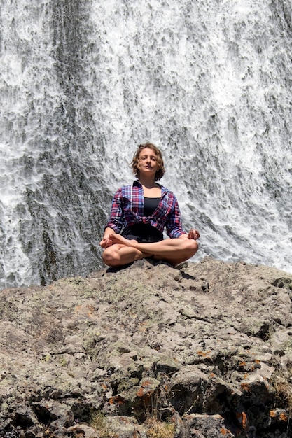 A garota está envolvida em ioga em um fundo de pose de lótus de cachoeira