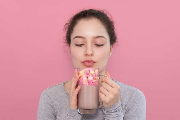 A garota está prestes a beber chocolate quente com marshmallows em um fundo rosa.