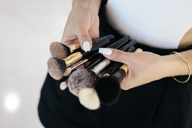 Foto a garota está segurando ferramentas de maquiagem maquiador profissional com uma bolsa de cinto com pincéis de maquiagem de borlas maquiador profissional fazendo maquiagem de modelo de glamour no trabalho