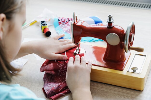 A garota está sentada à mesa e costurando em uma máquina de costura