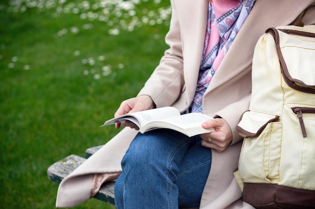 A garota está sentada em um banco de parque e lendo um livro