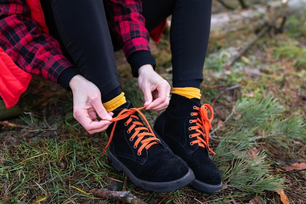 A garota está sentada em um tronco na floresta e amarrando cadarços brilhantes Conceito de trekking e caminhadas de viagem