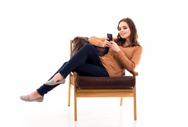 A garota está sentada em uma cadeira com um telefone nas mãos Comunicação online