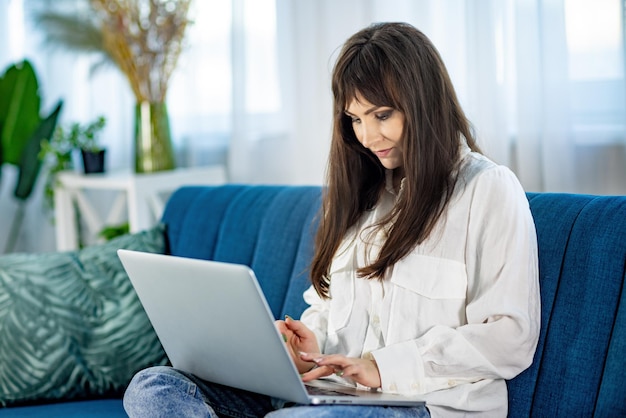 A garota está sentada no sofá e trabalhando em um laptop no apartamento